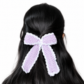Handmade lavender and white crochet bow hair clip attached to long black hair on a white background.